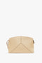 Beige leather handbag with a structured design and a wrist strap on the left side. The Victoria Clutch Bag In Sesame Leather by Victoria Beckham, Victoria’s favourite, has stitching details forming a geometric pattern on the front, resembling designs showcased in SS24 runway collections.