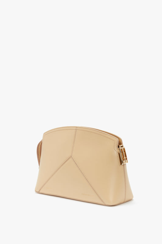 A Victoria Clutch Bag In Sesame Leather by Victoria Beckham with a geometric design and a gold buckle on one side, placed against a white background, reminiscent of Victoria's favourite SS24 runway style.