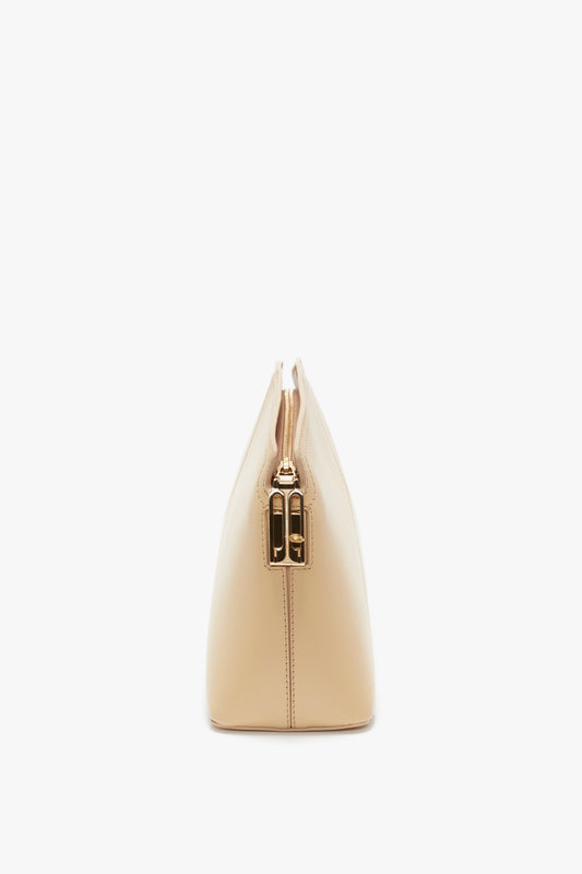 Side view of a beige triangular Victoria Clutch Bag In Sesame Leather with a compact design, crafted from glossy calf leather and featuring a gold-tone metallic zipper closure on top. Victoria’s favorite accessory from the SS24 runway collection by Victoria Beckham.