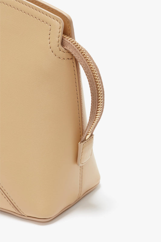 Close-up of a beige glossy calf leather clutch bag with a gold zipper and stitching detail on a white background, reminiscent of the Victoria Beckham Victoria Clutch Bag In Sesame Leather from the SS24 runway.