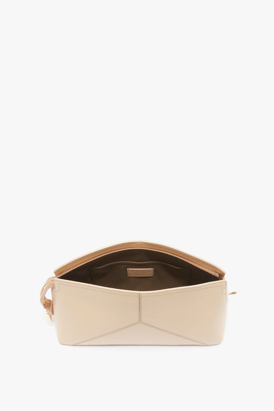A beige leather shoulder bag with its top zipper open, revealing a brown fabric-lined interior and a small internal pocket, embodies elements of Victoria Beckham's Victoria Clutch Bag In Sesame Leather from the SS24 runway.