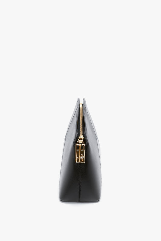 Side view of a Victoria Beckham Victoria Clutch Bag In Black Leather, made from glossy calf leather, featuring a gold zipper and a structured, minimalist silhouette.