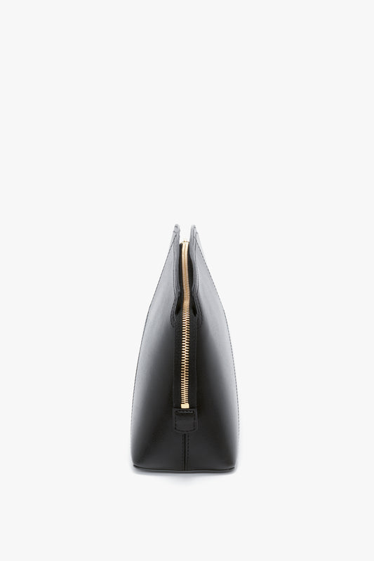 Side view of a Victoria Beckham Victoria Clutch Bag In Black Leather with a structured silhouette, featuring black glossy calf leather and a visible golden zipper at the top.