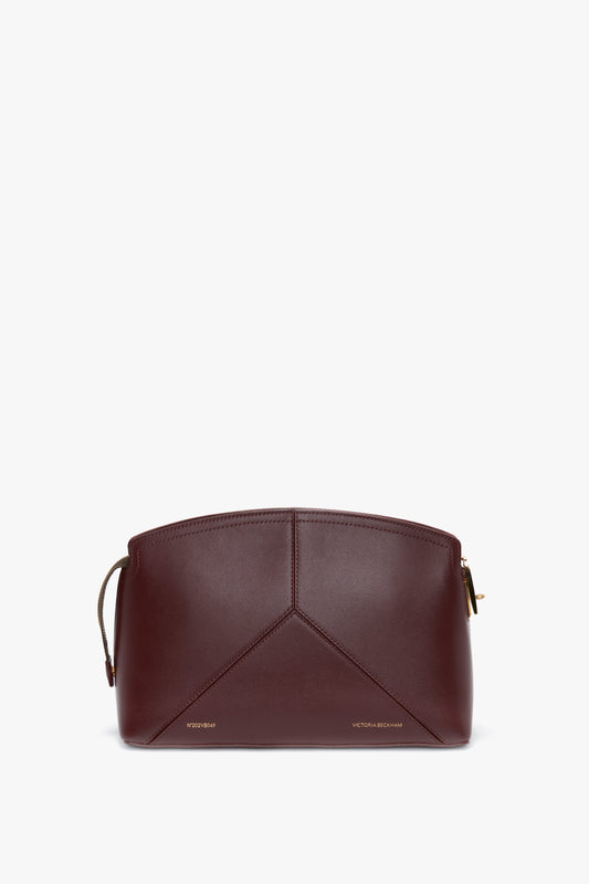 A structured, burgundy leather Victoria Clutch Bag In Burgundy Leather with minimalistic stitching, a zipper closure, and a subtle Victoria Beckham logo at the bottom, featuring a stylish branded padlock.