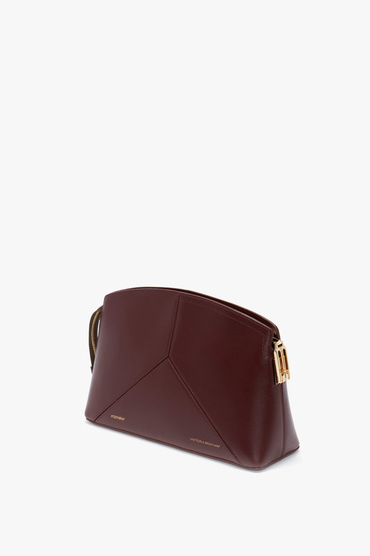 A Victoria Clutch Bag In Burgundy Leather with a structured geometric design and gold hardware, featuring the Victoria Beckham logo on the front and a distinctive branded padlock.