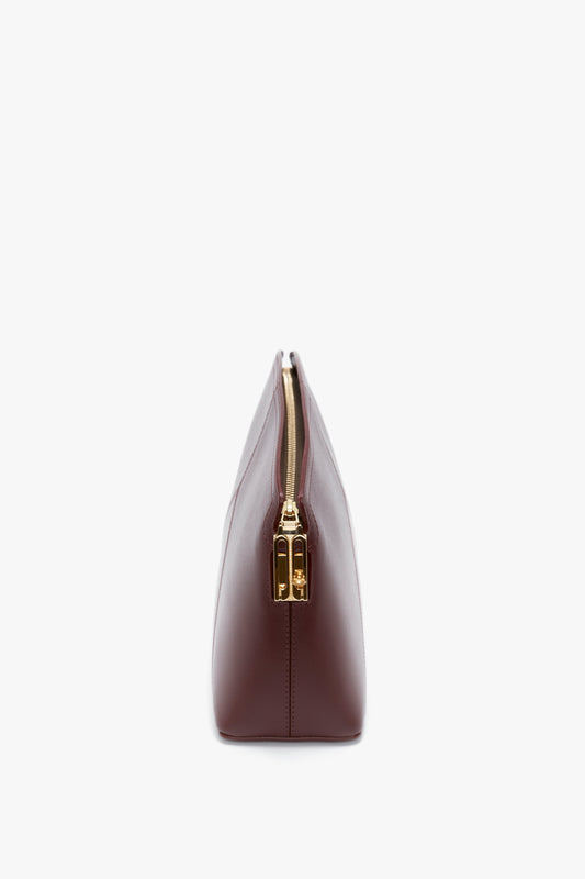 Side view of a closed, Victoria Clutch Bag In Burgundy Leather by Victoria Beckham with a gold zipper and a structured design against a white background.