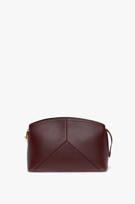 A **Victoria Clutch Bag In Burgundy Leather** with geometric stitching on the front and a zipper closure at the top. The bag boasts a structured design with clean lines, complemented by a branded padlock that adds a touch of sophistication. This exquisite piece is crafted by **Victoria Beckham**.