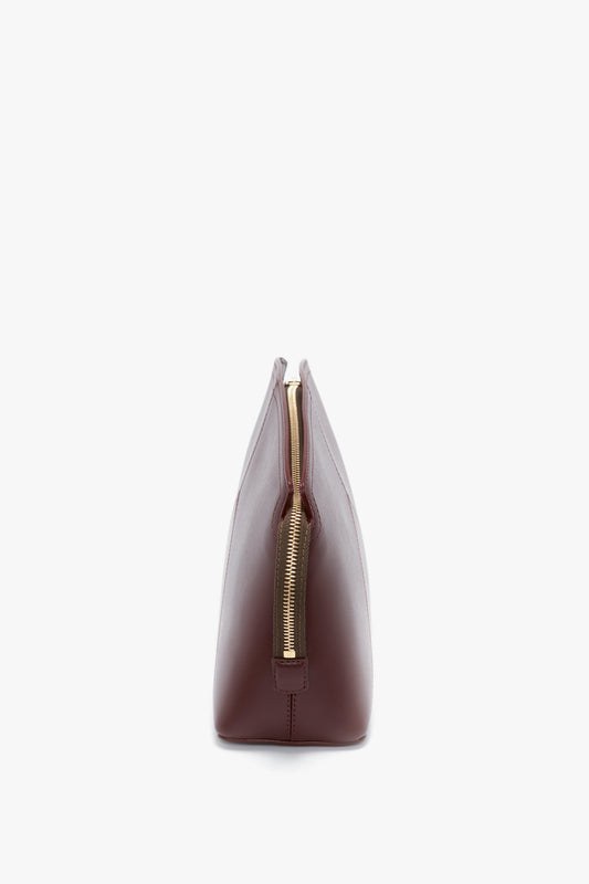 Side view of a Victoria Clutch Bag In Burgundy Leather by Victoria Beckham with a gold zipper and a structured design.