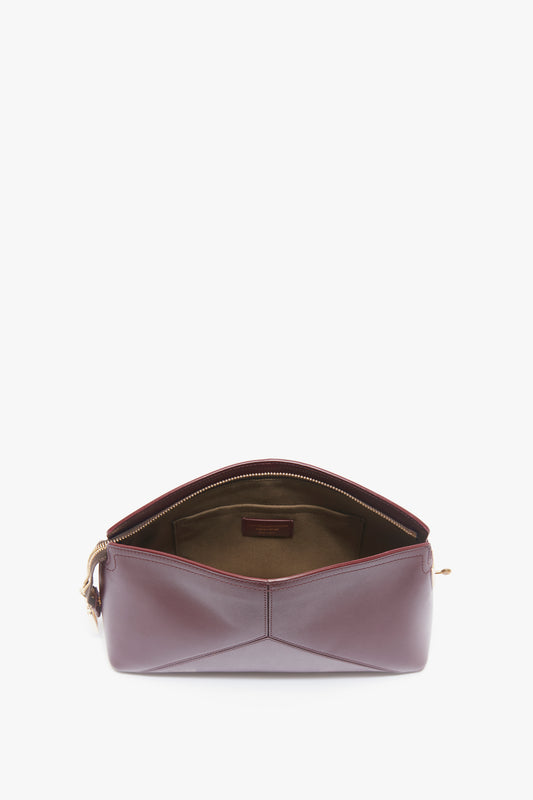 A Victoria Clutch Bag In Burgundy Leather by Victoria Beckham open with a visible beige interior, featuring a zipper closure and a structured design.