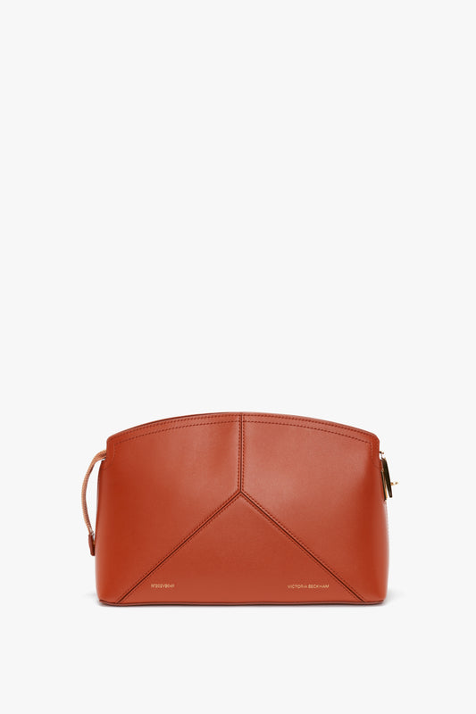 A brown, structured leather handbag with a geometric design, gold zipper, and a small strap on the side - the Victoria Clutch Bag In Tan Leather by Victoria Beckham is a true embodiment of elegance. Made from glossy calf leather, this piece doubles as an exquisite clutch bag for any sophisticated occasion.