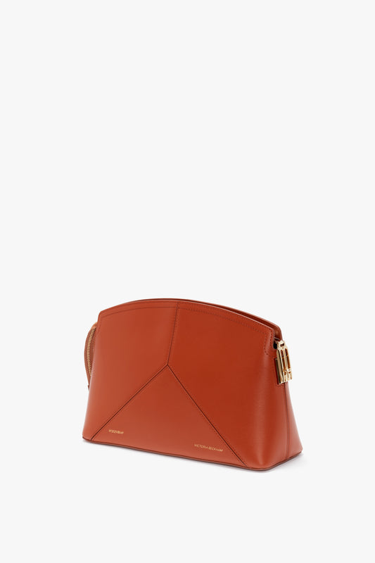A sleek, tan Victoria Beckham Victoria Clutch Bag In Tan Leather featuring clean, geometric lines and gold-tone hardware on the side. Crafted from glossy calf leather, this clutch bag exudes elegance and modern sophistication.