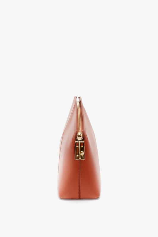 Side view of a glossy calf leather Victoria Clutch Bag In Tan Leather with a gold zipper closure on a white background, exuding the elegance synonymous with Victoria Beckham.