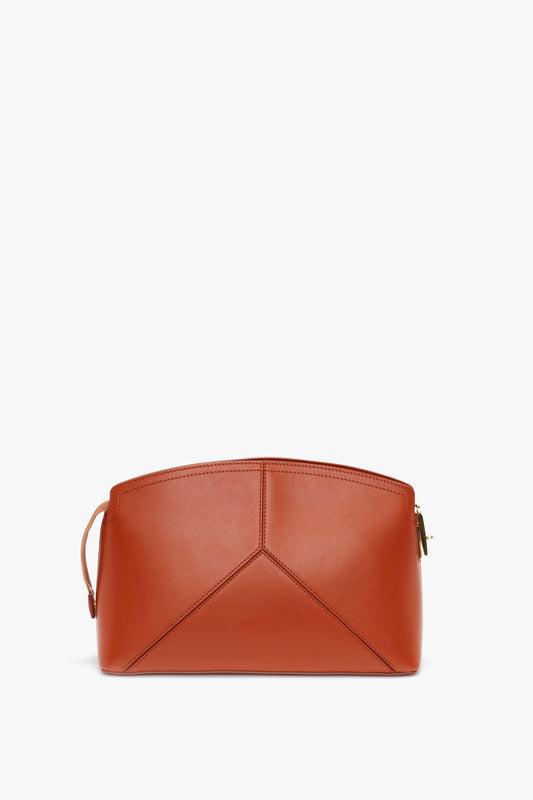 A structured, medium-sized brown leather handbag with a geometric design, a top zipper closure, and a slim wrist strap on the side, reminiscent of the Victoria Beckham Victoria Clutch Bag In Tan Leather.