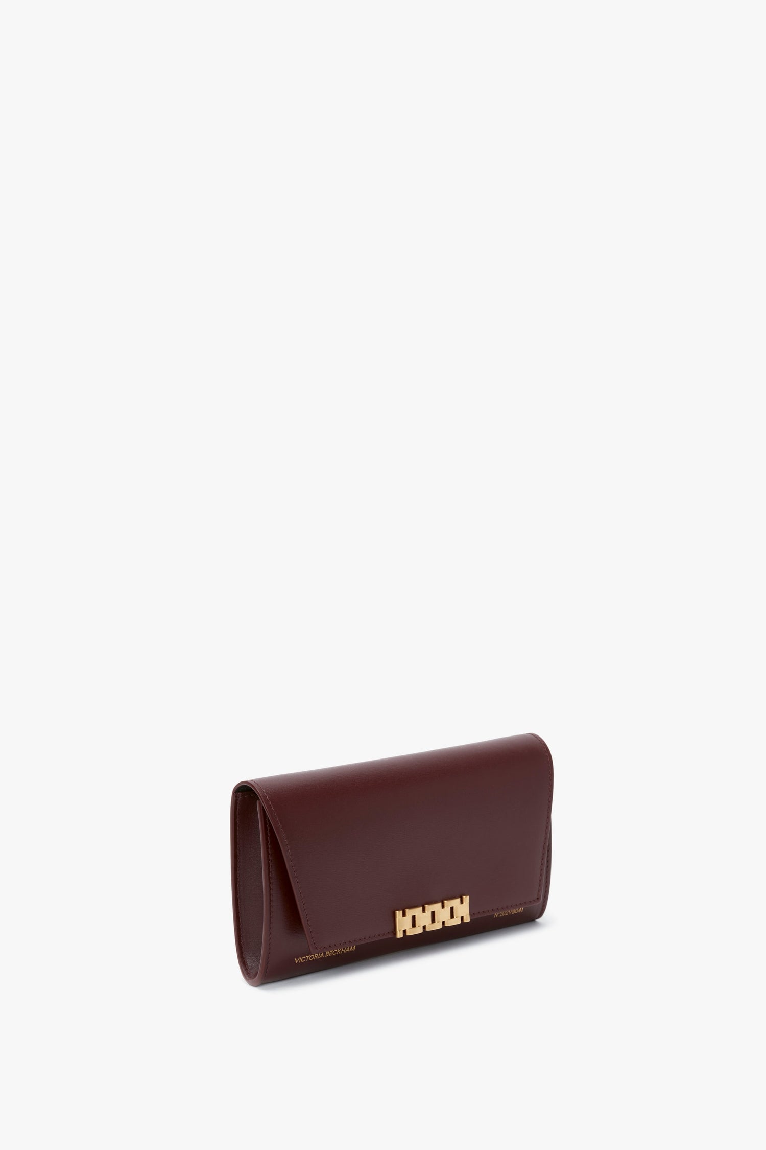 A sleek, Victoria Beckham Wallet On Chain In Burgundy Leather with a gold geometric clasp and chain closure on a plain white background.