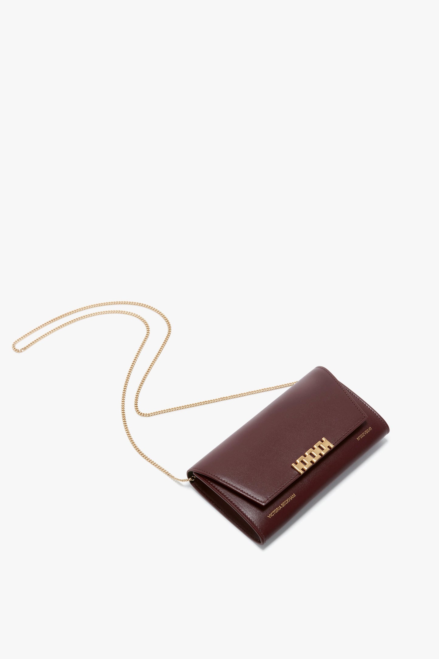 A Wallet On Chain In Burgundy Leather with a gold chain and gold-toned hardware, featuring a flap closure and the word "Victoria Beckham" on the front.