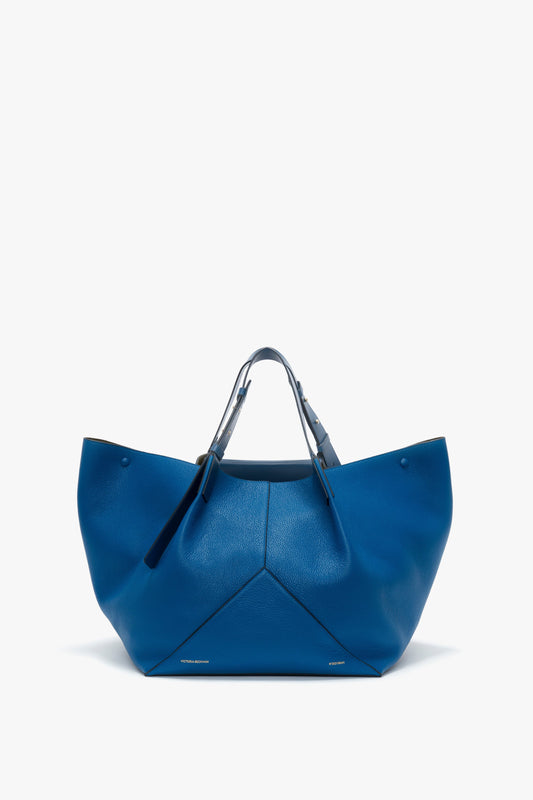 A Victoria Beckham W11 Medium Tote Bag In Vibrant Blue with a structured, geometric design crafted from grained leather, featuring dual top handles, placed against a white background.