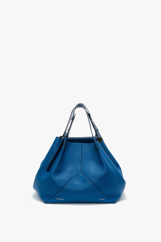 A large, vibrant blue W11 Medium Tote Bag In Vibrant Blue with a structured shape, crafted from grained leather, featuring two short handles and subtle stitching details on the front, set against a white background by Victoria Beckham.