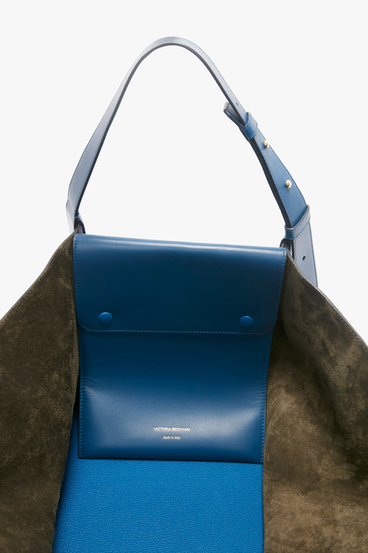 A close-up view of a vibrant blue and brown W11 Medium Tote Bag In Vibrant Blue with grained leather, featuring the name "Victoria Beckham" and "Made in Italy" inscribed on the interior.