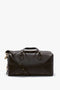 A dark brown calfskin duffel bag with short handles, a detachable shoulder strap, and gold hardware, reminiscent of the Victoria Beckham Medium Gym Bag In Chocolate Brown.