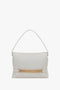 A Victoria Beckham Puffy Chain Pouch Bag With Strap In White Leather featuring a white design with a gold rectangular chain decoration near the bottom and a stylish detachable shoulder strap.