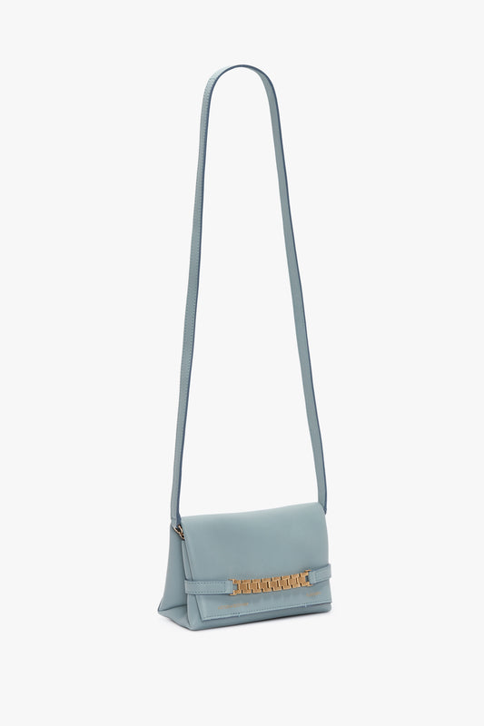Light blue leather shoulder bag with a gold-tone chain, standing upright against a white background. Victoria Beckham's Mini Chain Pouch With Long Strap In Ice Leather.