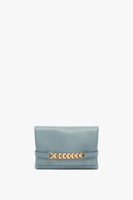 A small, rectangular, light blue Mini Chain Pouch Bag With Long Strap In Ice Leather featuring a gold-tone chain detail on the front and the brand name "Victoria Beckham" embossed on the lower right corner.