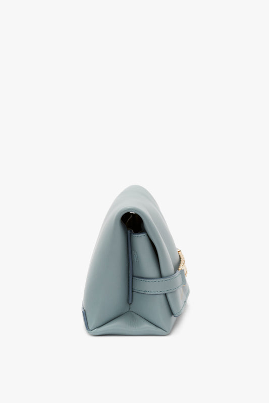 Side view of a light blue, rectangular Mini Chain Pouch Bag With Long Strap In Ice Leather with a flap closure and a gold-tone chain detail as the shoulder strap by Victoria Beckham.