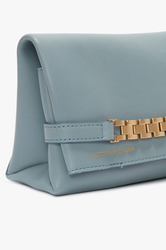 Close-up image of a light blue leather Mini Chain Pouch Bag With Long Strap In Ice Leather with a gold-tone chain detail on the front and "Victoria Beckham" embossed in gold letters.