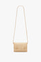 A beige Victoria Beckham Mini Chain Pouch With Long Strap In Sesame Leather, featuring a decorative chain detail on the front and suede lining.