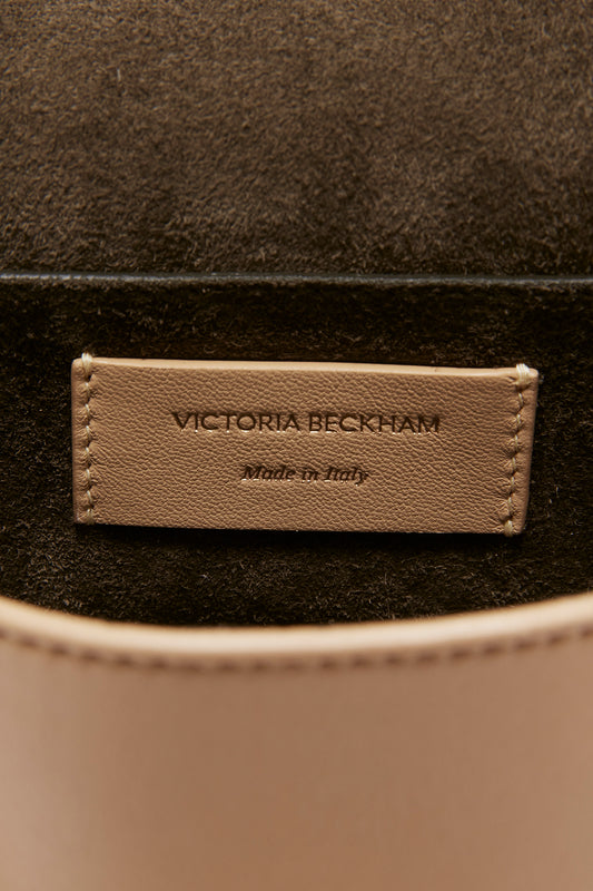 Close-up of a Victoria Beckham brand label on a Mini Pouch With Long Strap In Sesame Leather handbag, with the words "made in Italy" inscribed below.