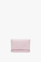 A rectangular, light pink Mini Chain Pouch Bag With Long Strap In Orchid Leather by Victoria Beckham with a smooth texture and a gold-tone chain is displayed against a white background.