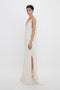 A woman stands against a white background, wearing an elegant off-white gown with asymmetrical ruffled layers and a crepe back satin high slit by Victoria Beckham's Exclusive Asymmetric Bias Frill Dress In Ivory.