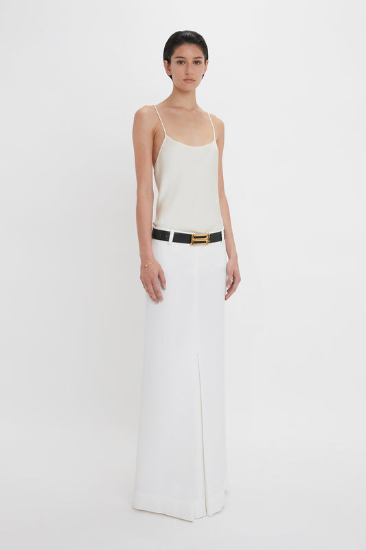 A person is standing against a white background, wearing an *Exclusive Cami Top In Ivory* by *Victoria Beckham* and a long white skirt with a black belt.
