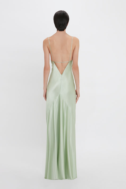 Woman from behind wearing an elegant Victoria Beckham Exclusive Low Back Cami Floor-Length Dress In Jade with a low back and delicate crisscross straps.