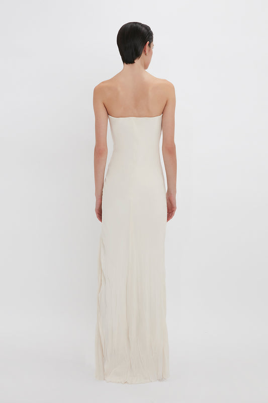 Woman in an elegant strapless sweetheart neckline Victoria Beckham gown, viewed from behind against a plain white background.