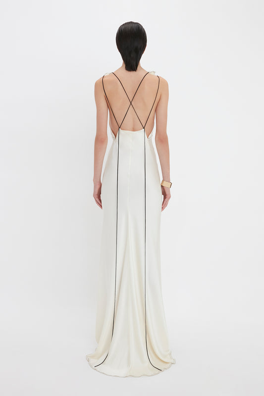 Person in a Victoria Beckham Gathered Shoulder Floor-Length Cami Gown in Ivory with thin black straps crisscrossing the back, standing against a plain white background.