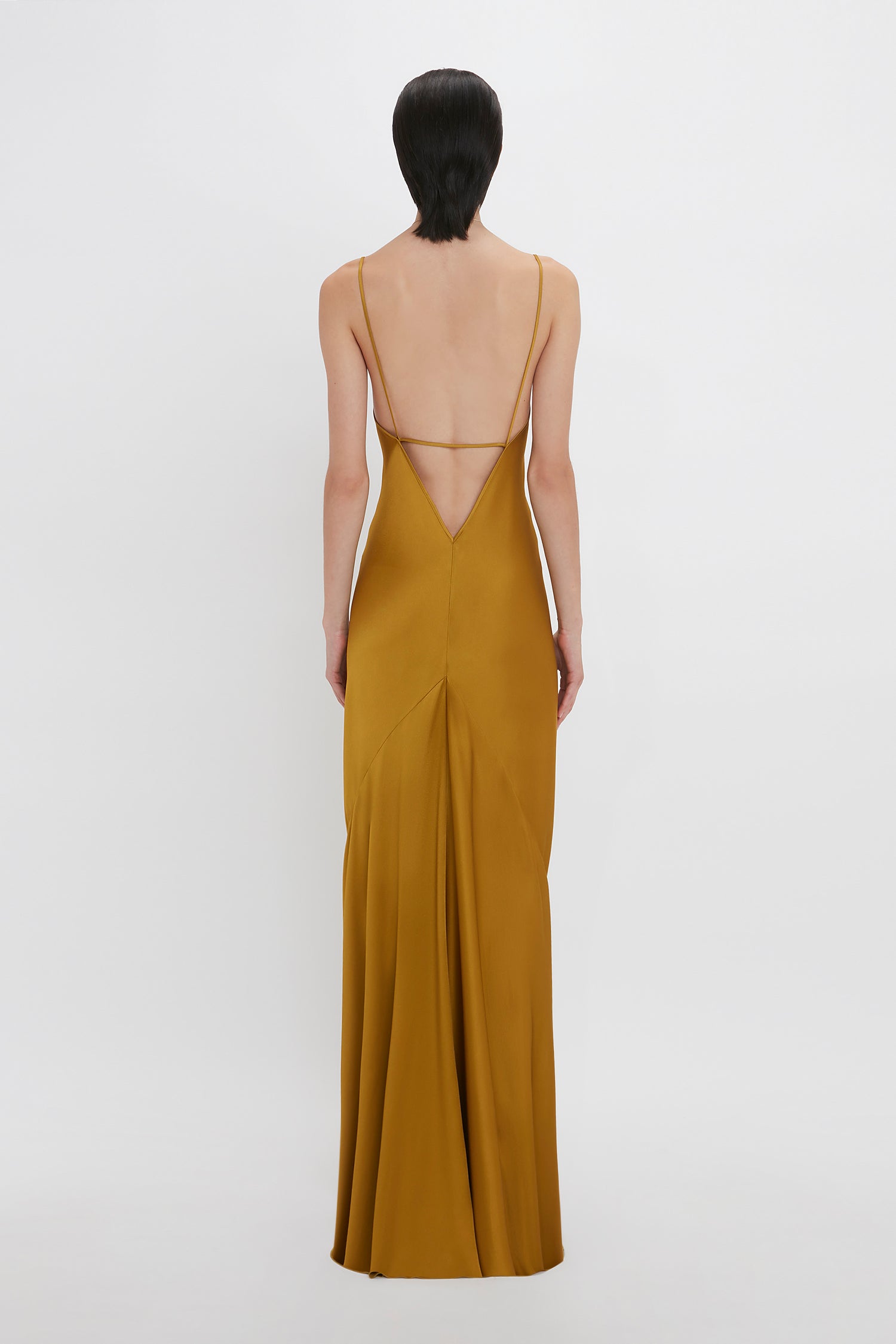 A person in a Victoria Beckham Low Back Cami Floor-Length Dress In Harvest Gold stands facing away against a white background.