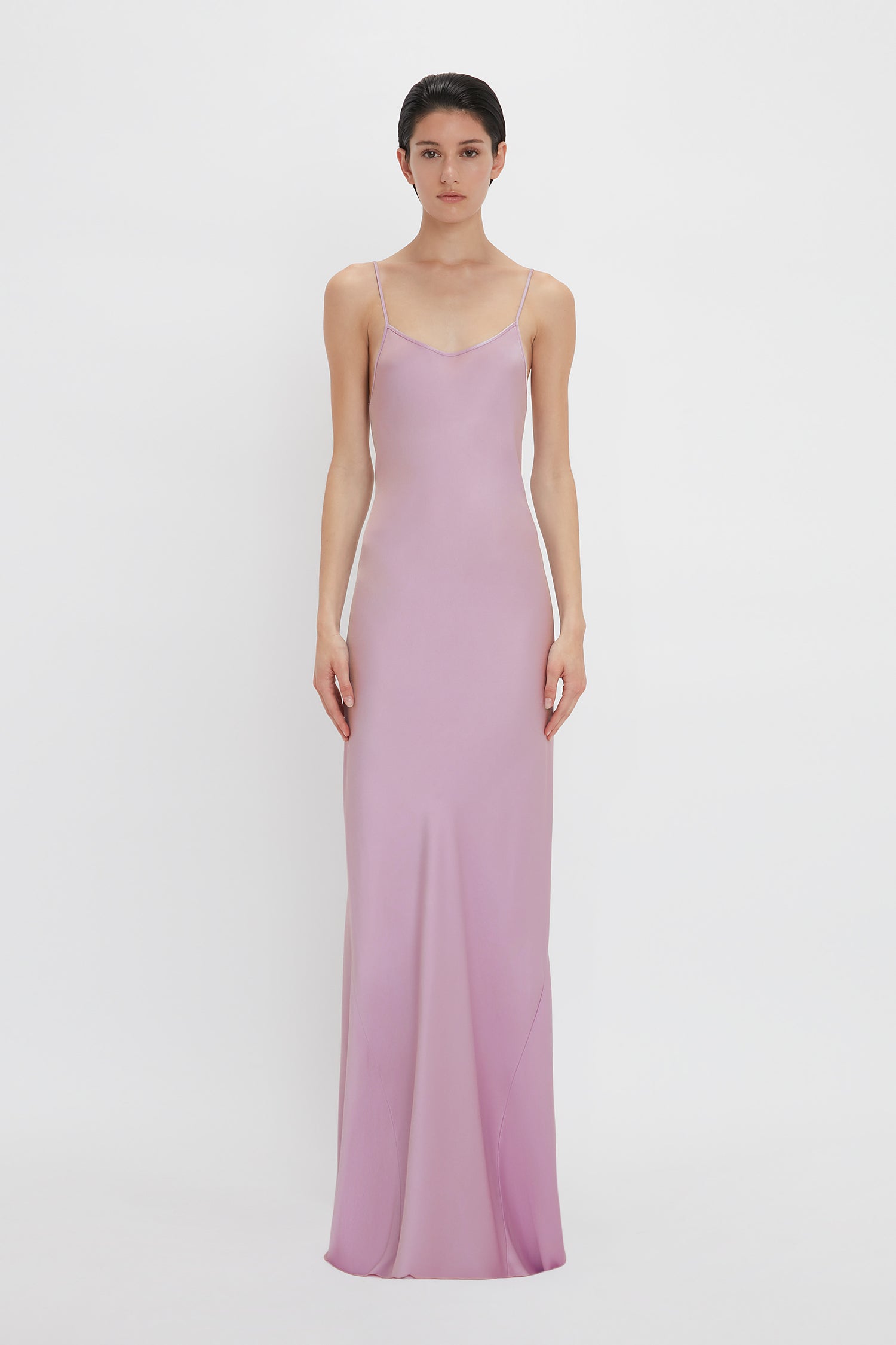 A person is standing wearing a Victoria Beckham Low Back Cami Floor-Length Dress In Rosa with thin straps, showcasing a sensuous silhouette against a plain white background.