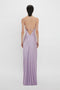 Rear view of a person wearing the Victoria Beckham Low Back Cami Floor-Length Dress In Petunia with spaghetti strap detailing, reminiscent of 1990s style, standing against a plain white background.