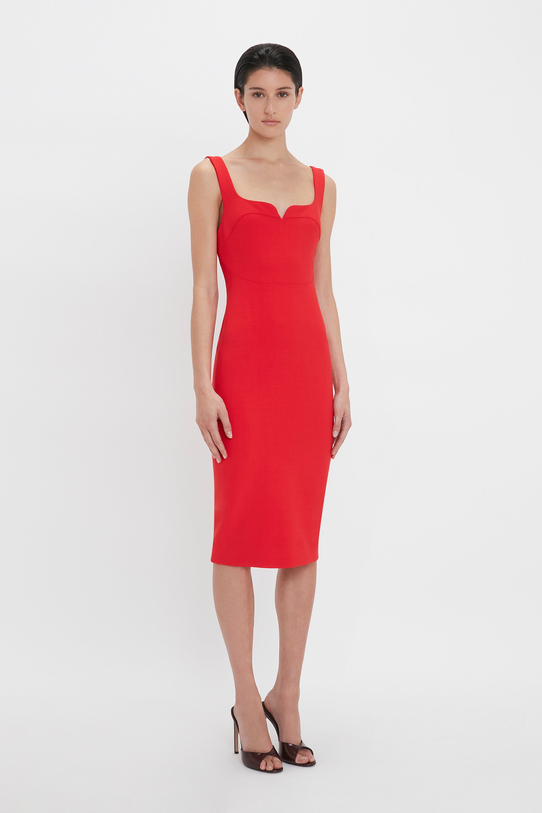 A person stands against a white background wearing a Sleeveless Fitted T-Shirt Dress In Bright Red by Victoria Beckham and black high heels.