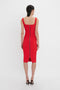 A person in a Sleeveless Fitted T-Shirt Dress In Bright Red by Victoria Beckham standing with their back to the camera, showcasing a visible zipper running from the neckline to the knee-length hem. Made from double wool crepe, the dress has wide shoulder straps.