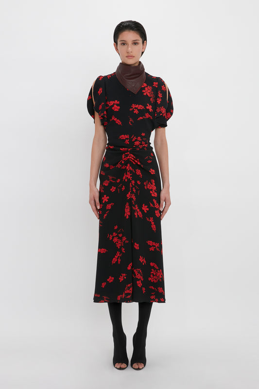 Person standing against a plain white background, wearing a fit-and-flare silhouette Gathered Waist Midi Dress In Sci-Fi Black Floral by Victoria Beckham, black tights, black peep-toe shoes, and a brown scarf.