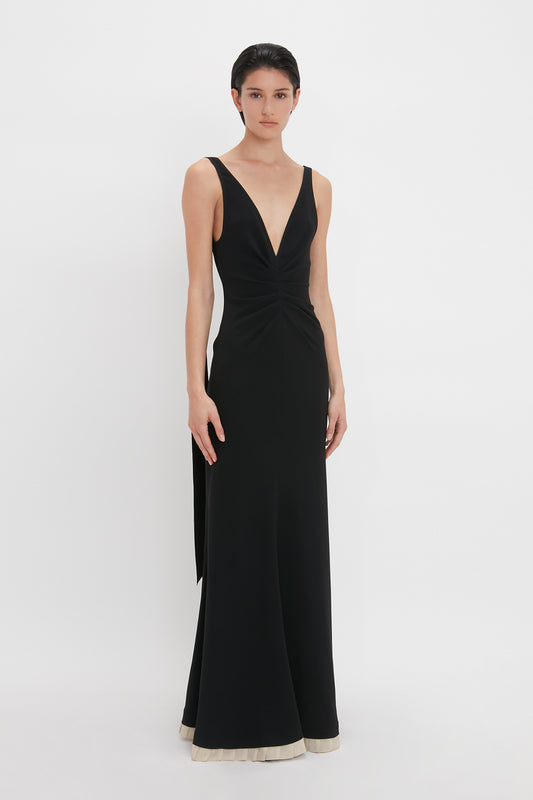 Person standing against a white background, wearing the Victoria Beckham V-Neck Gathered Waist Floor-Length Gown In Black.