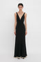 A person wearing the Victoria Beckham V-Neck Gathered Waist Floor-Length Gown In Black.