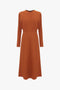 A long-sleeve, ankle-length, rust-colored Dolman Midi Dress In Russet by Victoria Beckham with a simple, elegant design made from fluid cady fabric, featuring a fitted waist, voluminous underarm drape, and a round neckline.