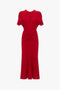 A red, short-sleeve, knee-length dress with a round neckline and a gathered knot detail at the waist, reminiscent of the Exclusive Gathered Waist Midi Dress In Carmine by Victoria Beckham.