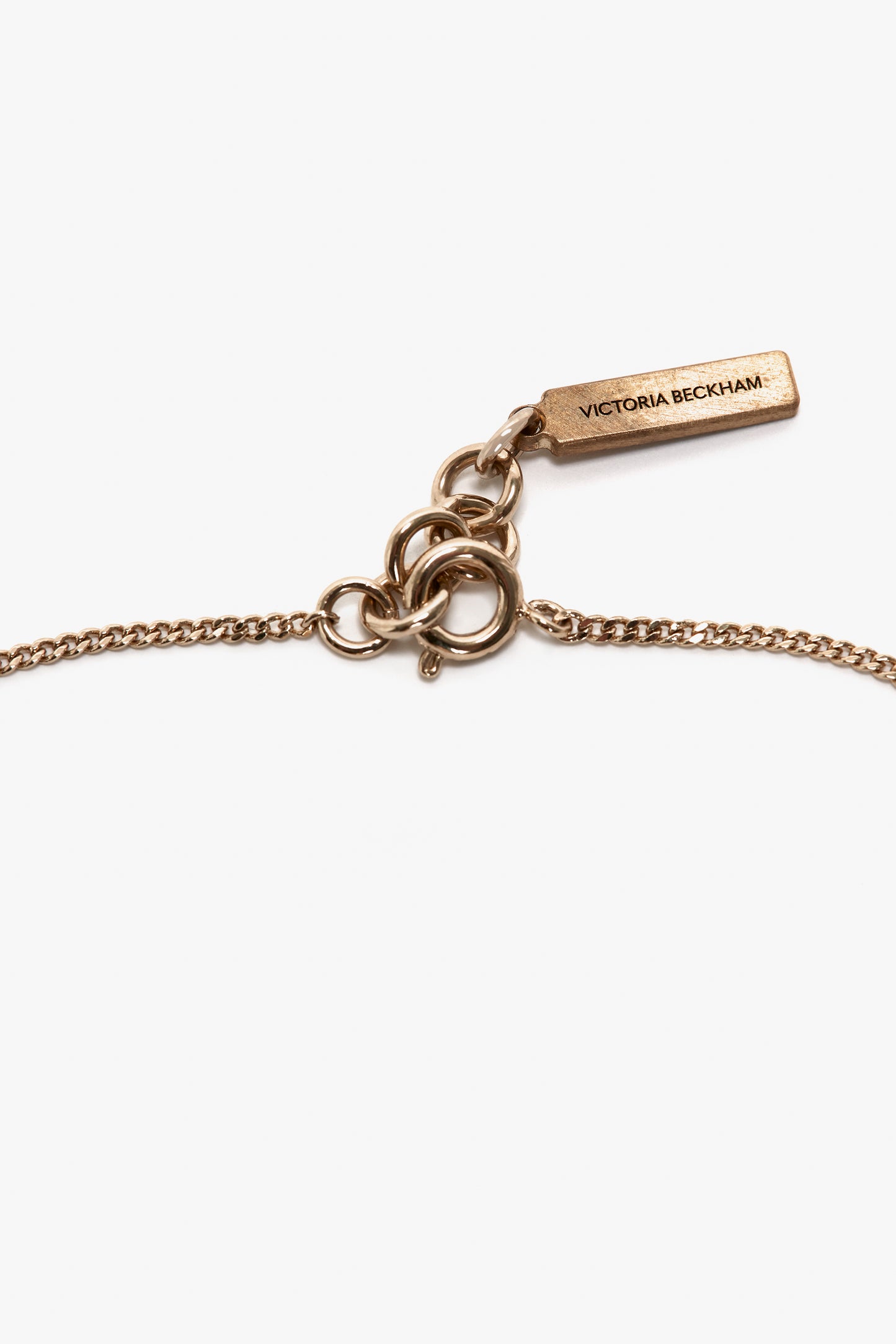 Close-up of an Exclusive Camellia Flower Bracelet In Gold clasp featuring interlocking rings and a rectangular tag engraved with the text "Victoria Beckham".