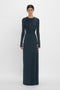 Person standing in a full-length dark blue Ruched Detail Floor-Length Gown In Midnight by Victoria Beckham with long sleeves, embodying understated glamour against a plain white background.