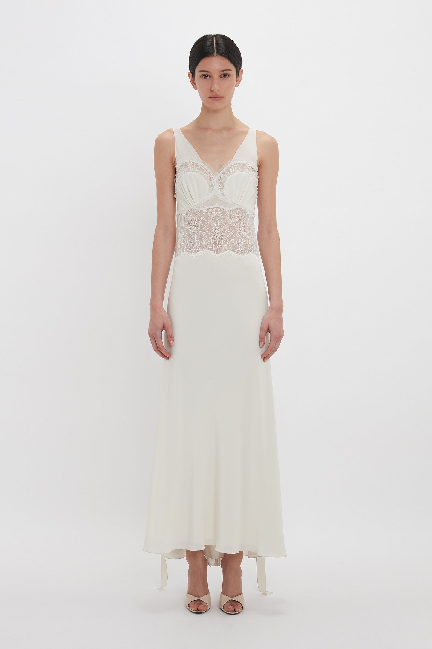 A person is wearing a sleeveless, floor-length, Ruffle Detail Midi Dress in Ivory by Victoria Beckham, standing against a plain white background.