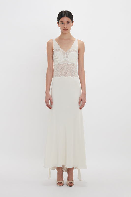 A person is wearing a sleeveless, floor-length, Ruffle Detail Midi Dress in Ivory by Victoria Beckham, standing against a plain white background.